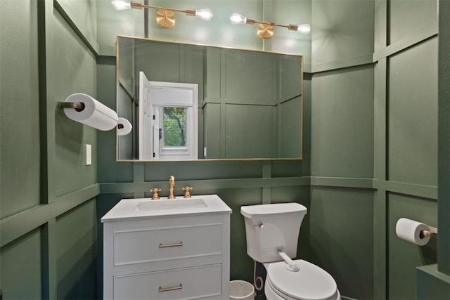 bathroom with vanity, a decorative wall, and toilet