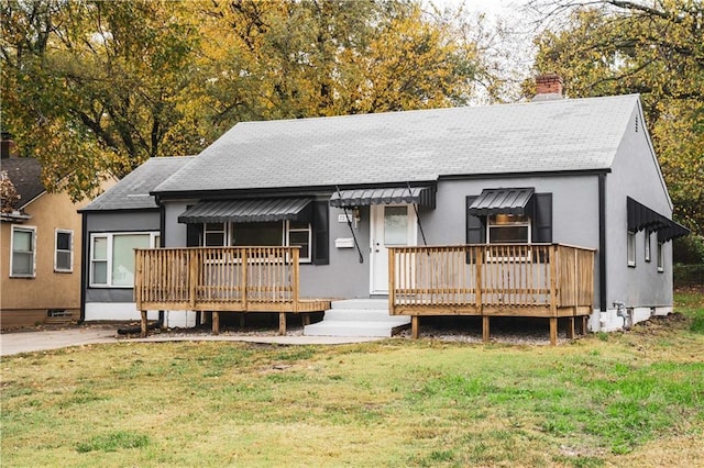 view of front facade featuring a chimney, a wooden deck, a shingled roof, and a front lawn