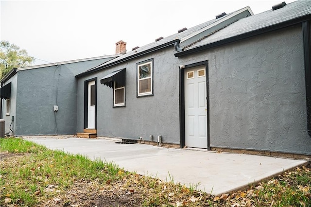 rear view of property featuring a patio, central AC, a chimney, and stucco siding