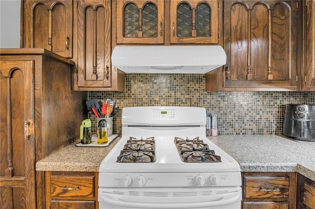 kitchen with white range with gas cooktop, range hood, light countertops, glass insert cabinets, and backsplash