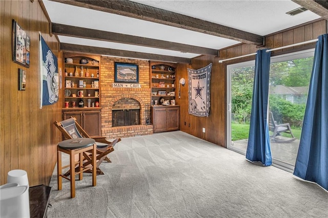 living area with wood walls, beam ceiling, carpet flooring, a brick fireplace, and built in shelves