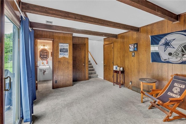 sitting room with wood walls, beam ceiling, stairs, and carpet flooring
