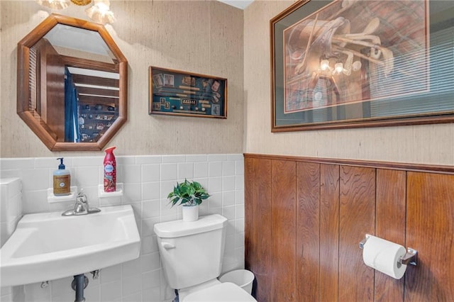 bathroom featuring a wainscoted wall, toilet, a sink, and tile walls