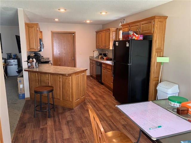 kitchen featuring a kitchen breakfast bar, brown cabinetry, a peninsula, dark wood-type flooring, and black appliances