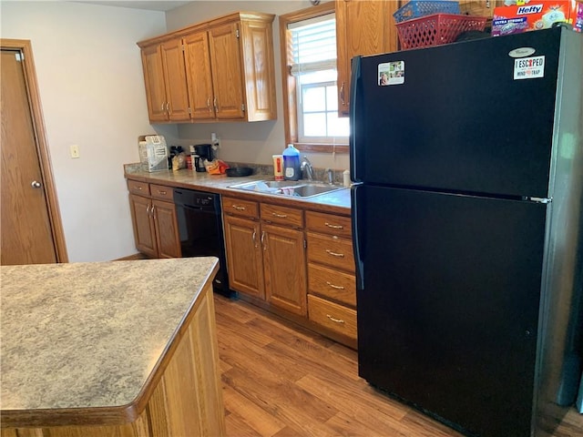 kitchen featuring a sink, light countertops, brown cabinetry, light wood-type flooring, and black appliances