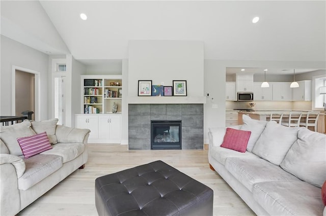 living area with recessed lighting, vaulted ceiling, a tile fireplace, and light wood-style floors