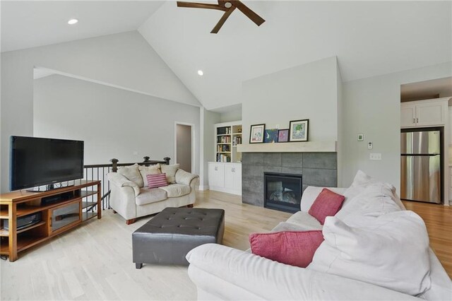 living room featuring light wood-style floors, high vaulted ceiling, recessed lighting, a tile fireplace, and a ceiling fan
