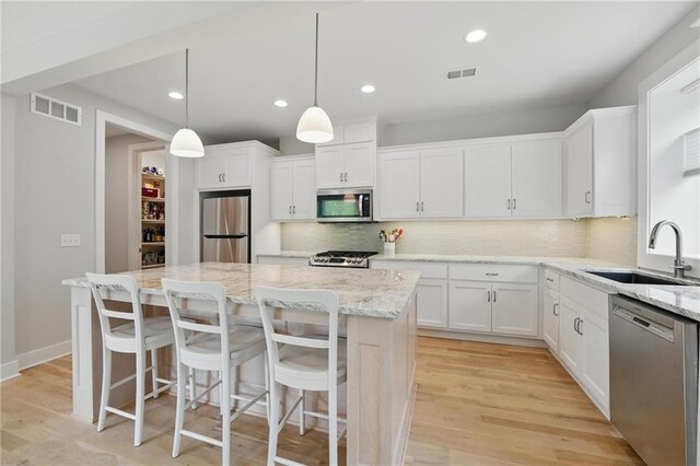 kitchen with a sink, a center island, stainless steel appliances, decorative backsplash, and visible vents
