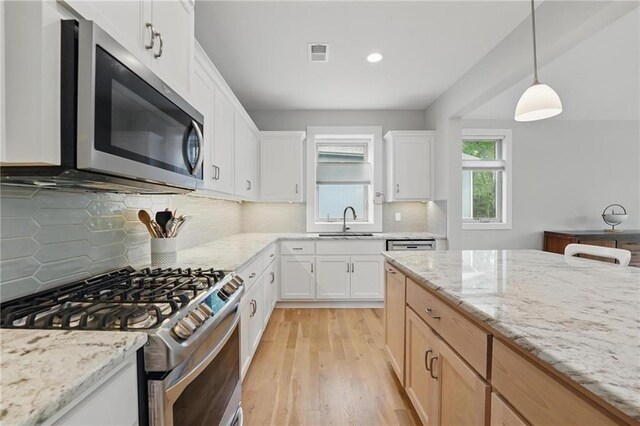 kitchen with visible vents, appliances with stainless steel finishes, light stone countertops, a sink, and light wood-style floors
