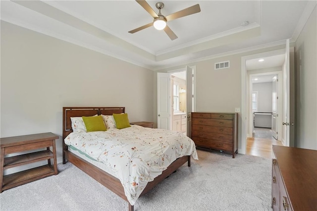 bedroom featuring crown molding, light carpet, a raised ceiling, ensuite bathroom, and visible vents
