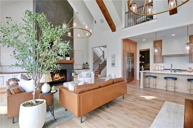 living room featuring stairs, high vaulted ceiling, a notable chandelier, and light wood finished floors
