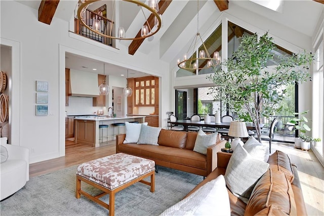 living room with beam ceiling, high vaulted ceiling, baseboards, a notable chandelier, and light wood-style flooring