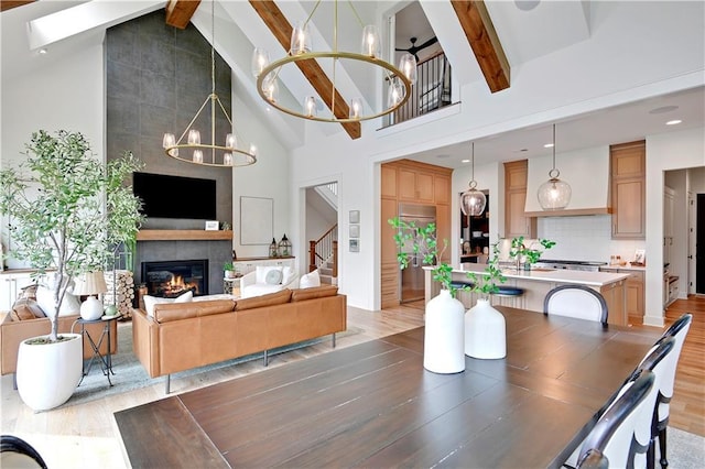 dining area with an inviting chandelier, beamed ceiling, light wood-style floors, stairway, and high vaulted ceiling