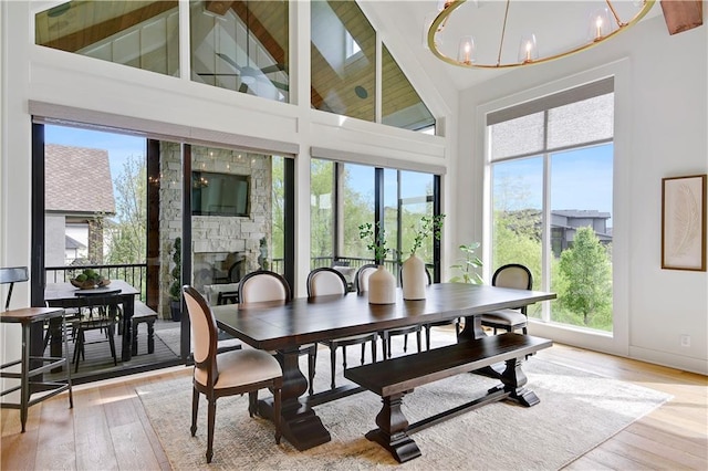 dining area featuring a fireplace, high vaulted ceiling, a chandelier, light wood-type flooring, and beamed ceiling