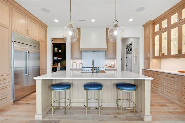 kitchen featuring light countertops, stainless steel built in fridge, light wood finished floors, and premium range hood