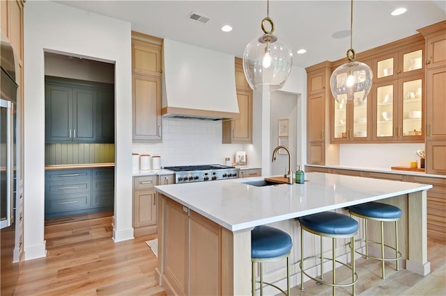 kitchen with a sink, light countertops, custom exhaust hood, light wood-style flooring, and an island with sink