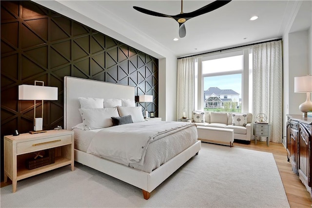 bedroom with light wood-type flooring, a ceiling fan, and a decorative wall