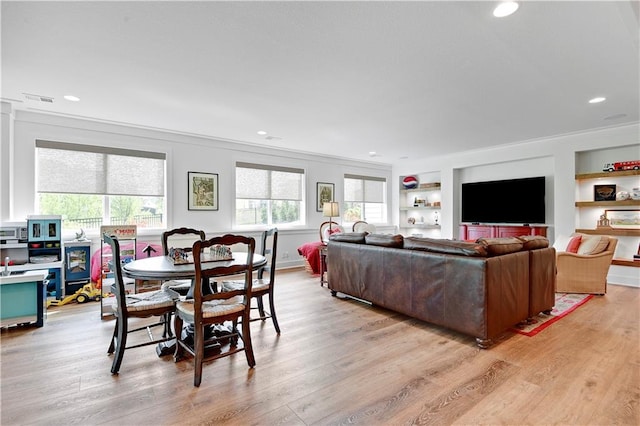 living area with visible vents, ornamental molding, built in features, and light wood finished floors