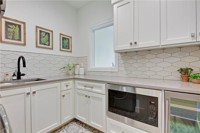 kitchen featuring wine cooler, light countertops, built in microwave, white cabinets, and a sink