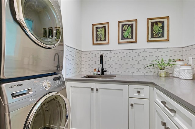 washroom with cabinet space, stacked washing maching and dryer, and a sink