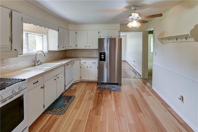 kitchen with decorative backsplash, a sink, light countertops, light wood-style floors, and white appliances