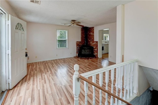 living area featuring ceiling fan, a wood stove, light wood-style floors, a textured ceiling, and visible vents
