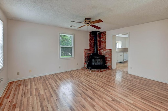 unfurnished living room with light wood-style floors, a wood stove, and a textured ceiling