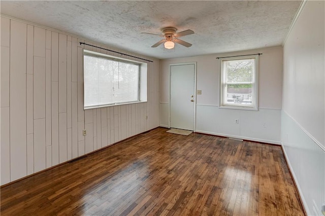 unfurnished room featuring a ceiling fan, a textured ceiling, wooden walls, and hardwood / wood-style floors
