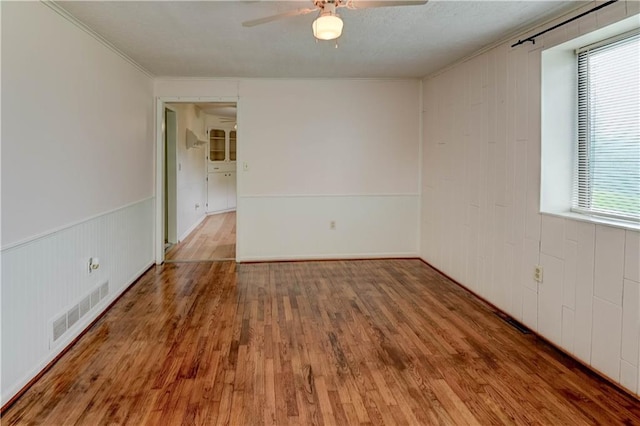 empty room with plenty of natural light, ceiling fan, wood finished floors, and visible vents