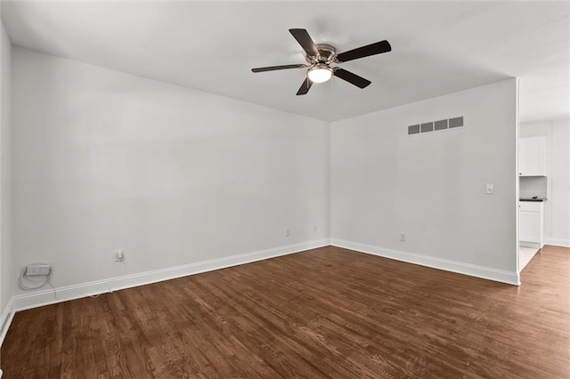 spare room featuring dark wood-style flooring, a ceiling fan, and baseboards
