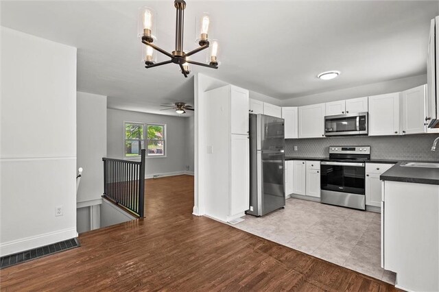 kitchen featuring stainless steel appliances, a chandelier, a sink, dark countertops, and white cabinets