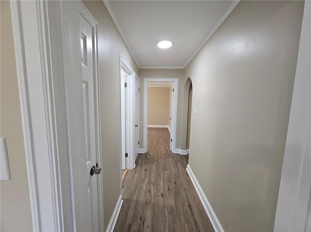 hallway with crown molding, arched walkways, baseboards, and dark wood-style floors