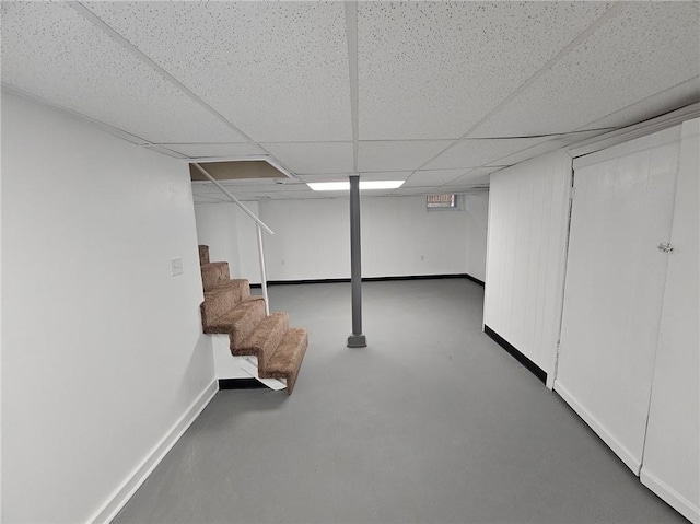 finished below grade area with stairway, baseboards, and a paneled ceiling