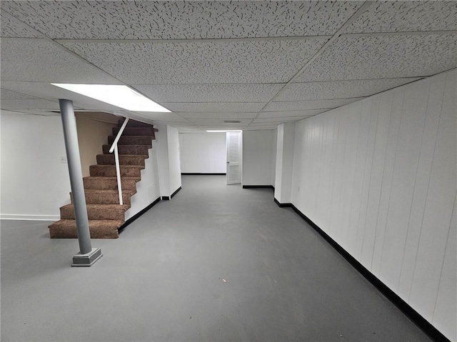 finished basement featuring baseboards, stairs, and a paneled ceiling