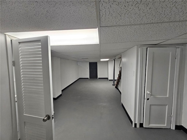 finished basement featuring baseboards, a paneled ceiling, and stairway