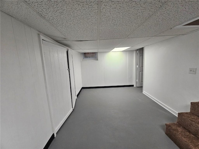 finished below grade area featuring stairway, baseboards, and a paneled ceiling