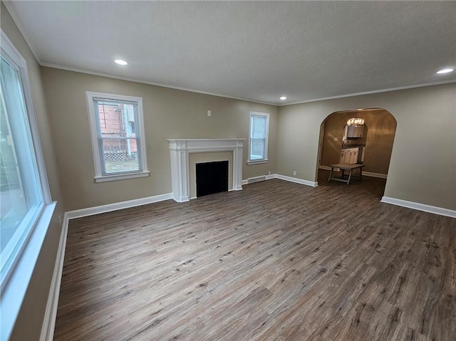 unfurnished living room with arched walkways, baseboards, ornamental molding, and wood finished floors