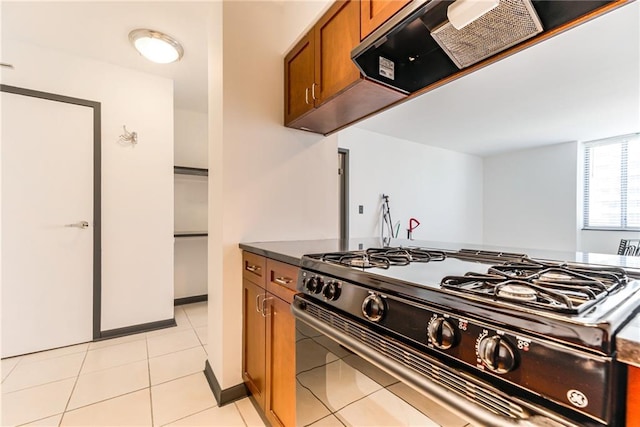 kitchen with brown cabinets, light tile patterned flooring, dark countertops, black range with gas stovetop, and extractor fan