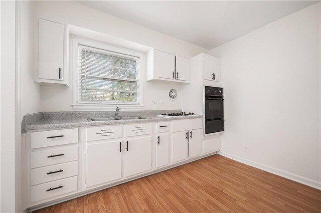 3525-3527 Bell St, Kansas City, MO 64111 - kitchen with light wood finished floors, a sink, black oven, light countertops, and white cabinets