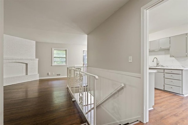 corridor featuring a sink, light wood-style flooring, a wainscoted wall, an upstairs landing, and visible vents