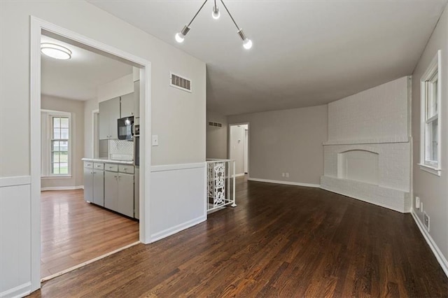 unfurnished living room with a brick fireplace, dark wood-style floors, and visible vents