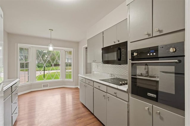 kitchen featuring backsplash, light wood-type flooring, light countertops, baseboards, and black appliances