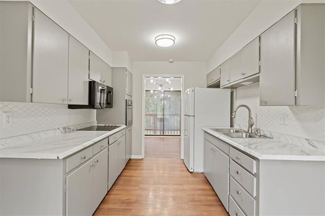 kitchen with a sink, light wood-style floors, light countertops, backsplash, and black appliances