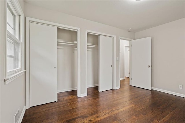 unfurnished bedroom featuring two closets, baseboards, visible vents, and wood finished floors