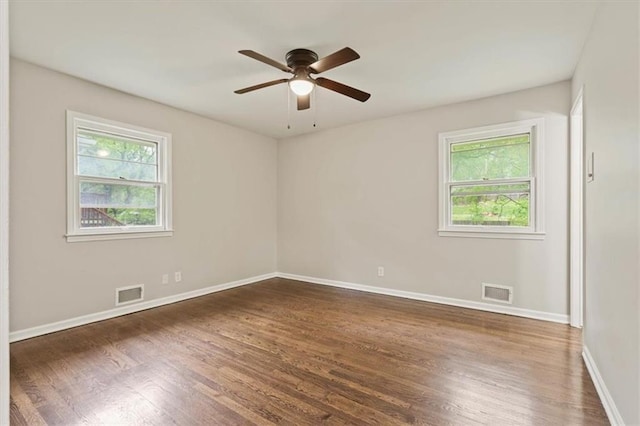 empty room featuring dark wood-style floors, visible vents, and plenty of natural light