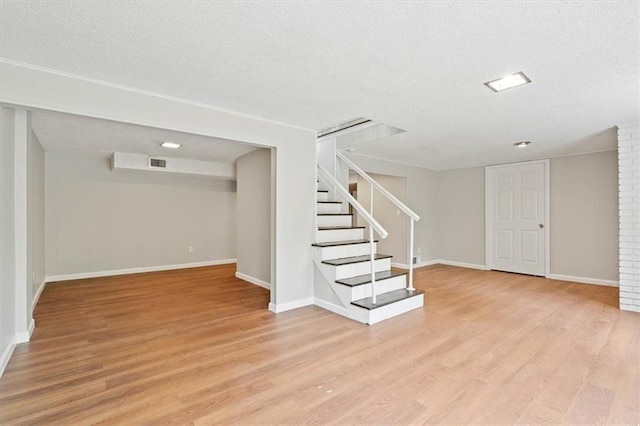 finished basement featuring a textured ceiling, light wood-style flooring, baseboards, visible vents, and stairway