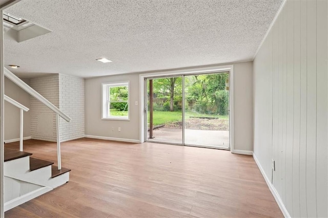 unfurnished living room featuring light wood-style floors, a textured ceiling, and stairway