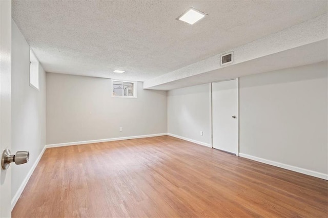 finished basement featuring a textured ceiling, baseboards, wood finished floors, and visible vents