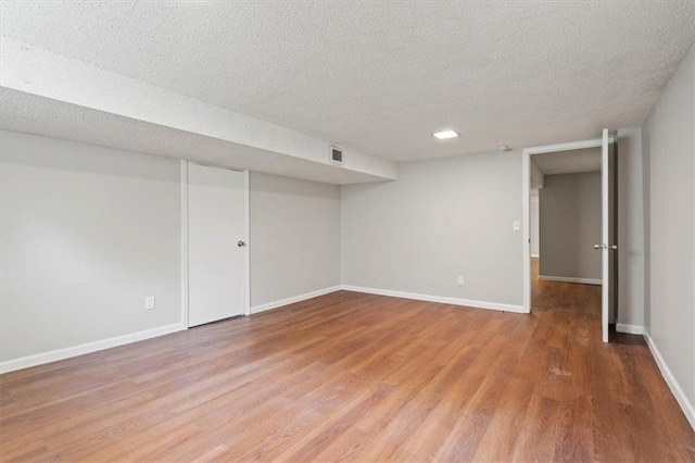 finished basement featuring a textured ceiling, baseboards, visible vents, and light wood-style flooring