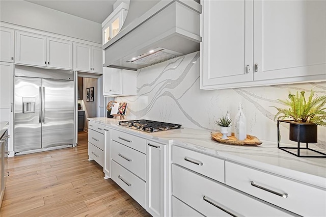 12605 W 170th St, Overland Park, KS 66221 - kitchen with appliances with stainless steel finishes, premium range hood, white cabinetry, light stone counters, and light wood finished floors